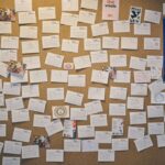 A corkboard covered with numerous handwritten notes and small cards, featuring various messages and drawings. There is a blue poster on the right side with white text and an origami bird illustration.