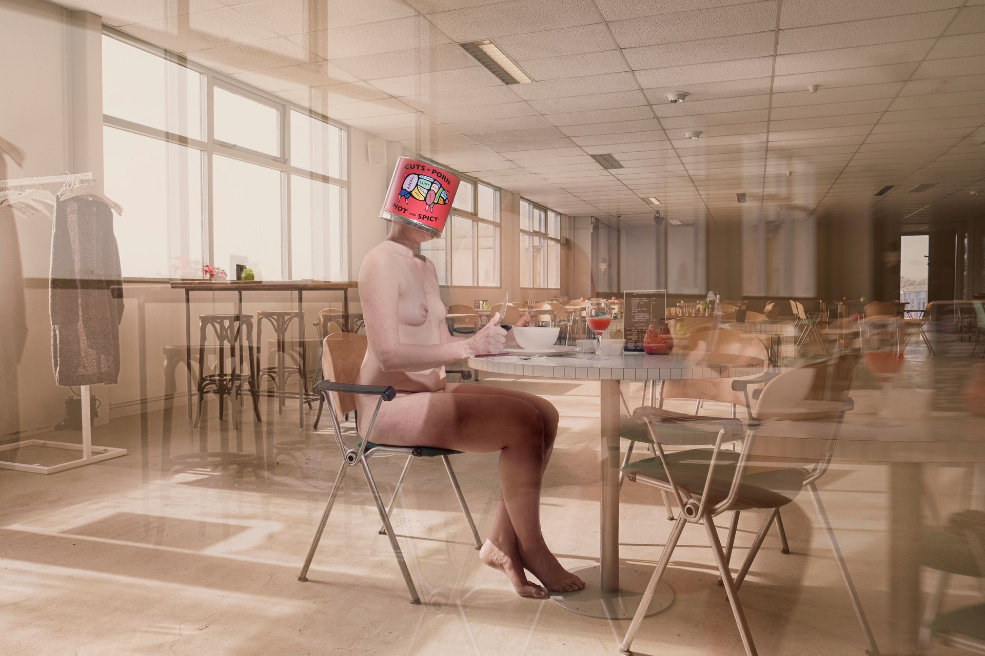 A nude person sits at a table in an empty room, eating from a bowl. Their head is replaced by the Lust box with colorful graphics—surreal and blurred, the image evokes motion or a dreamlike scene.
